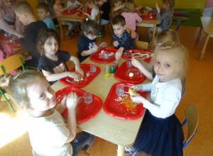 Dzieci siedzą przy stoliku i ugniatają nad tackami masę plastyczną.